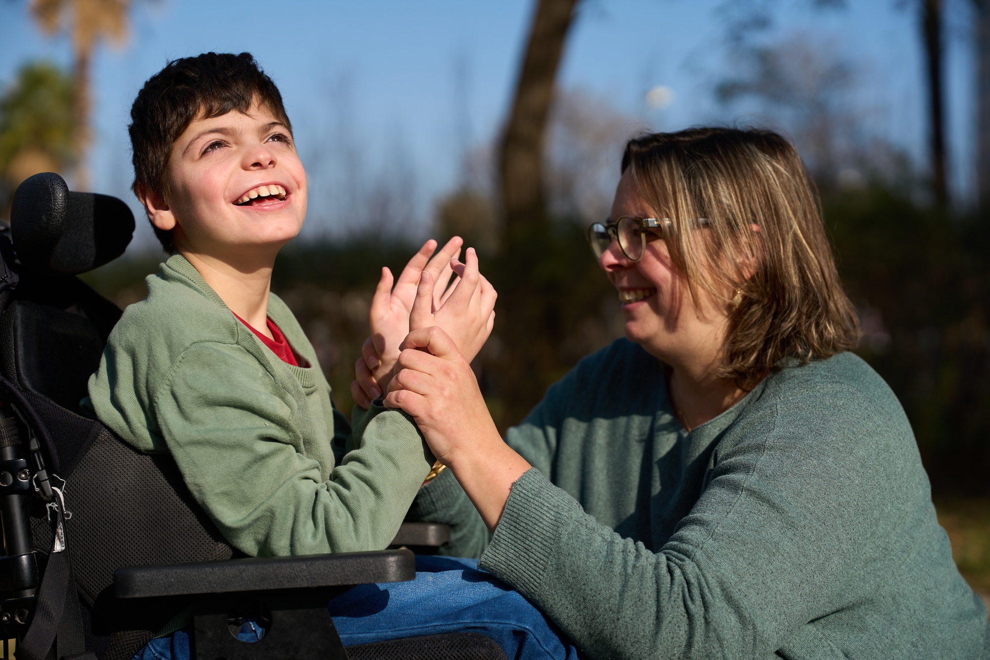 Therapist assisting child with disability in wheelchair outdoors - cerebral palsy concept