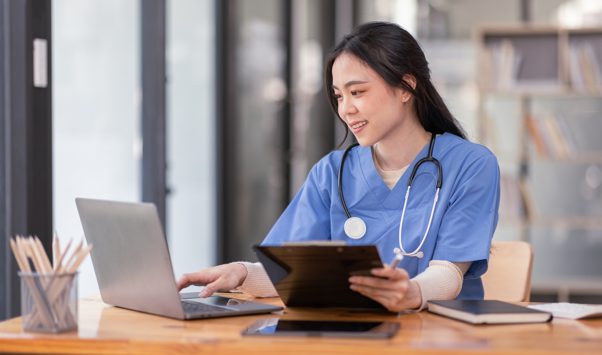 Portrait of Young Asian smiling female nurse working on laptop in private clinic, Positive emotional